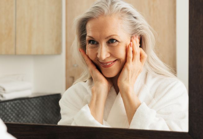 Female in bathrobe looking in mirror with hands on face