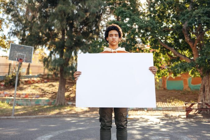 Male teenager holding a blank placard in an urban park