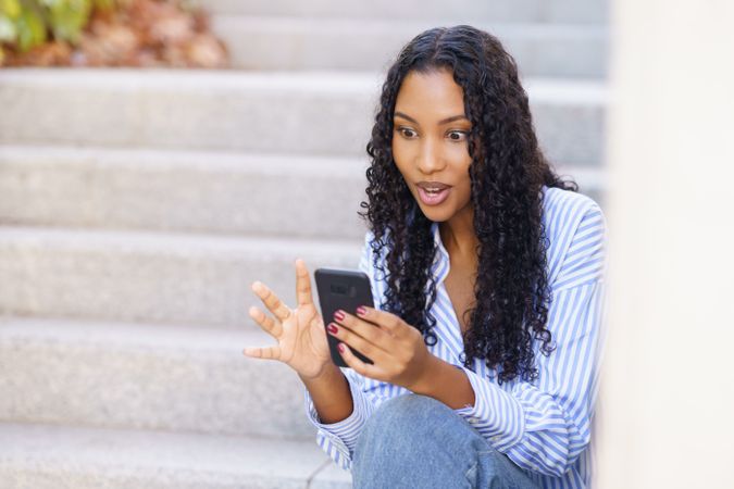 A young woman is happily engaged with her smartphone while sitting on outdoor steps