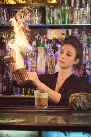 Female barkeeper making fire over cup while mixing cocktail