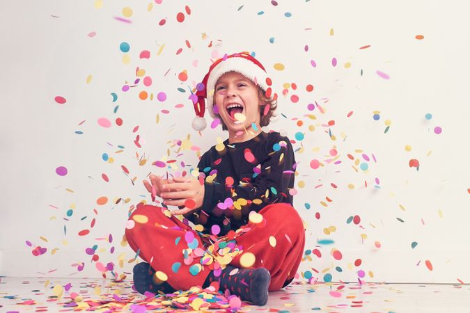 Smiling boy in Santa hat under colorful confetti