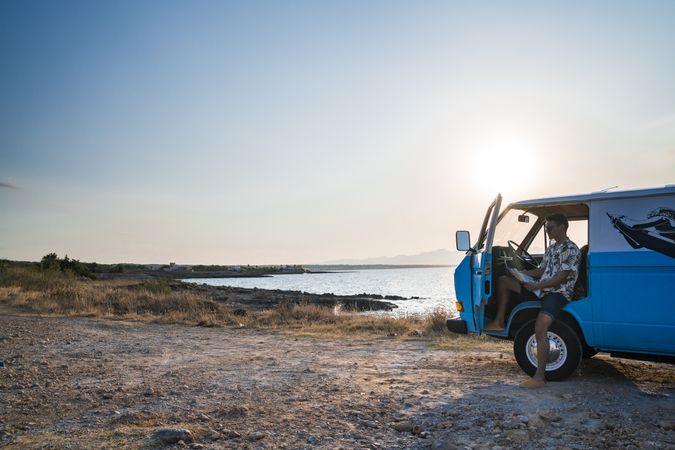 Adult man planing route for road trip while sitting in car on shore
