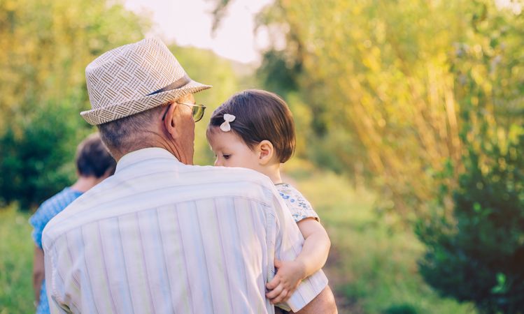 Back view of older man holding baby girl in his arms