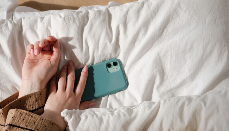 Hand holding smartphone on bed