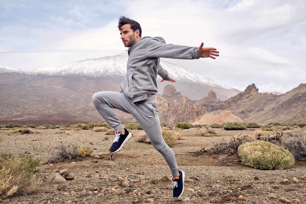 Young positive man in activewear jumping on rocky terrain