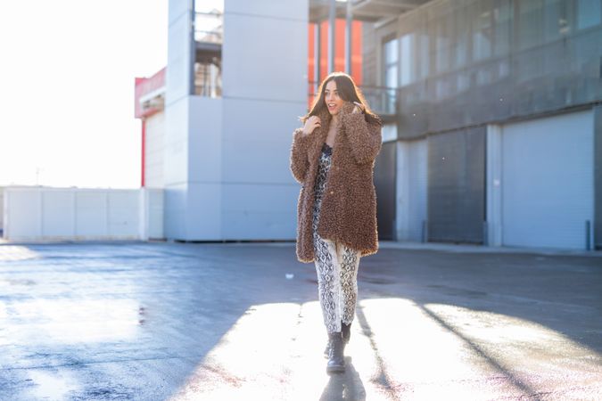 Cheerful woman wrapping in coat on street