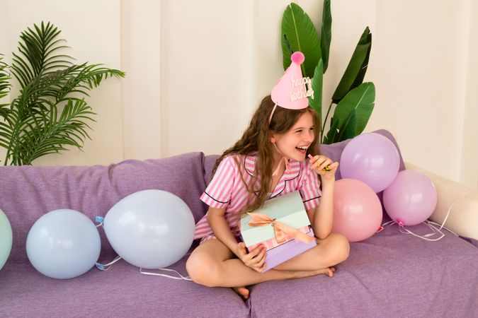 Girl laughing with party hat and holding birthday gifts.
