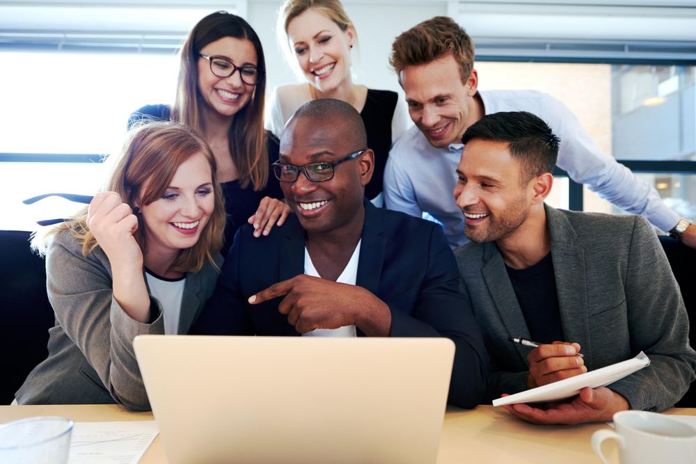 Laughing business associates huddled around a laptop in an office
