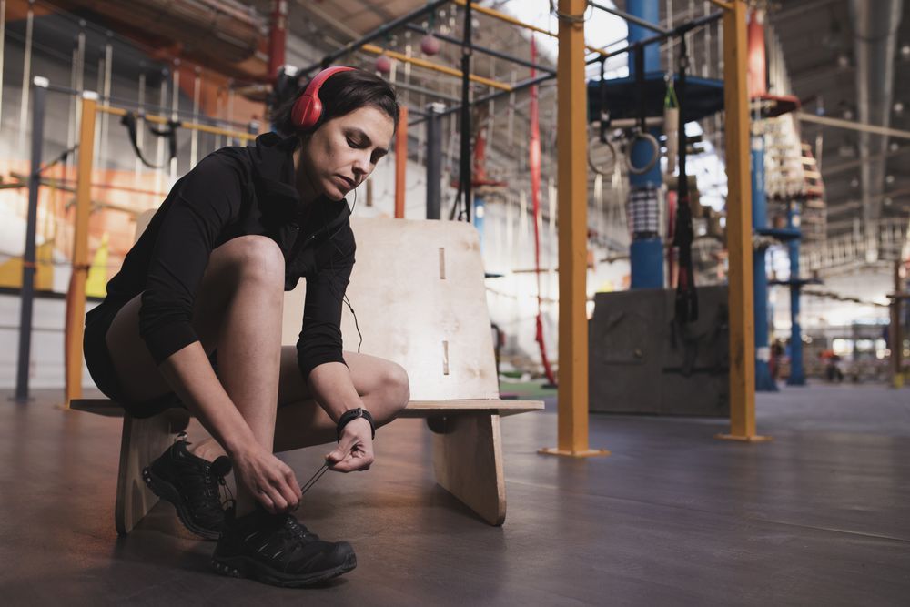 Smiling woman with headphones lacing shoe in gym
