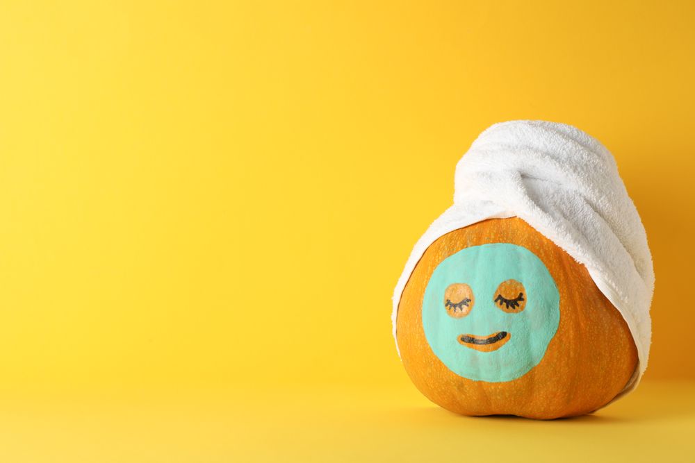 Pumpkin with facial mask and towel on yellow background, copy space