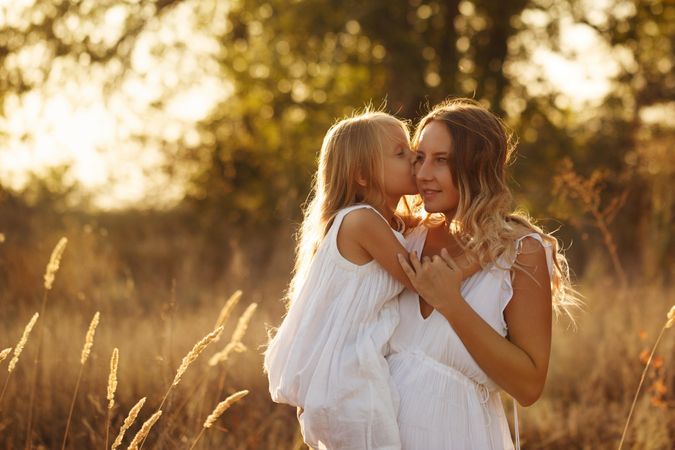 Little girl giving the woman carrying her a kiss in marsh at sunset