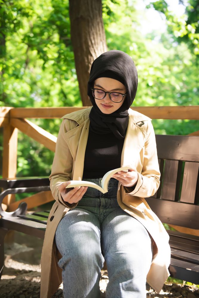Woman in headscarf engrossed in a book in the park