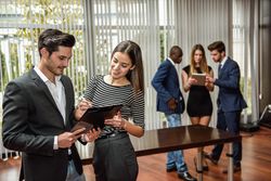 Two colleagues referring to clip board in busy office
