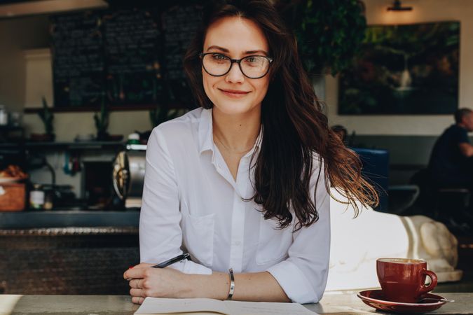Portrait of attractive female sitting at cafe with notebook and cup of coffee on table