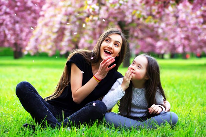 Two females sitting at a park and watching flower petals fall from trees