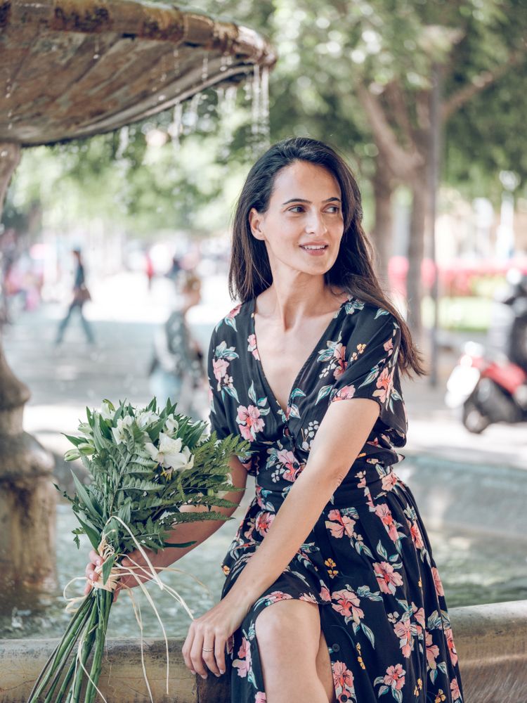 Charming female resting on edge of fountain with bouquet
