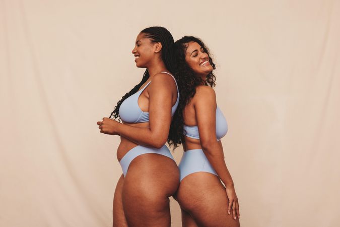 Two women wearing blue undergarments standing back to back in studio