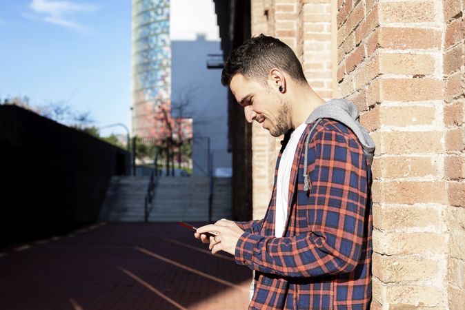 Young bearded male leaning on a brick wall while using a smartphone