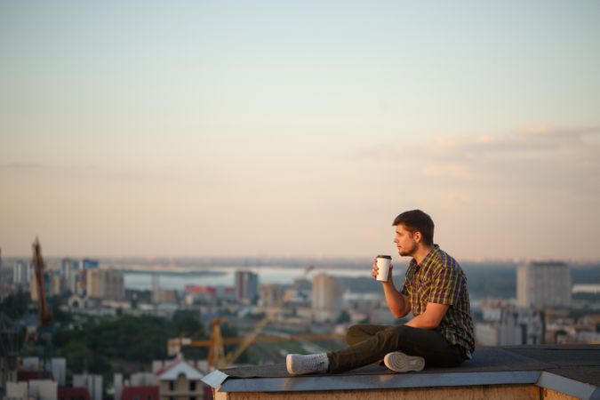 Side view of man perched on roof sipping coffee