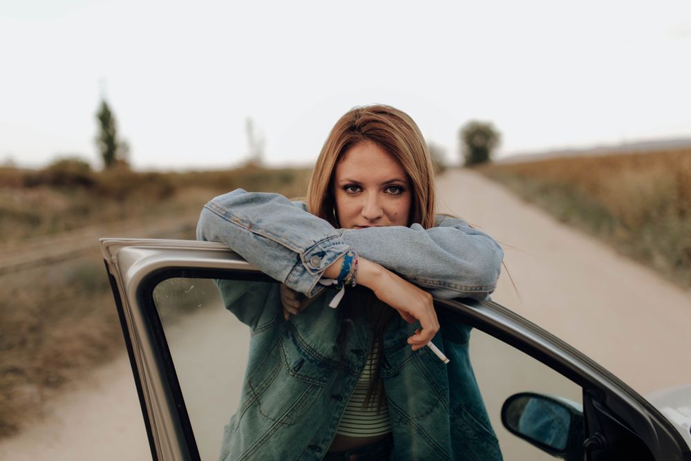 Modern woman with cigarette near car in nature