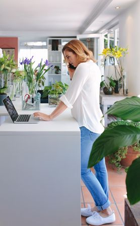 Female florist talking on phone and using laptop at flower shop