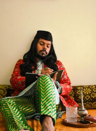Indian man with long hair sitting of floor and writing on a notebook