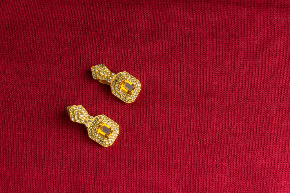 Beautiful shiny golden earrings with diamond studded Indian traditional design on a red velvet background