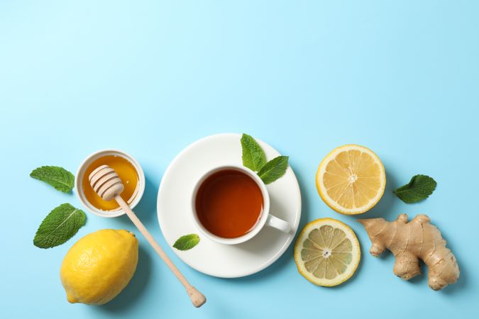 Flat lay. Cup of tea, lemon, ginger, mint, honey and dipper on blue background, copy space