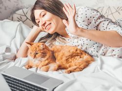 Cute ginger cat and woman lying in bed on video call