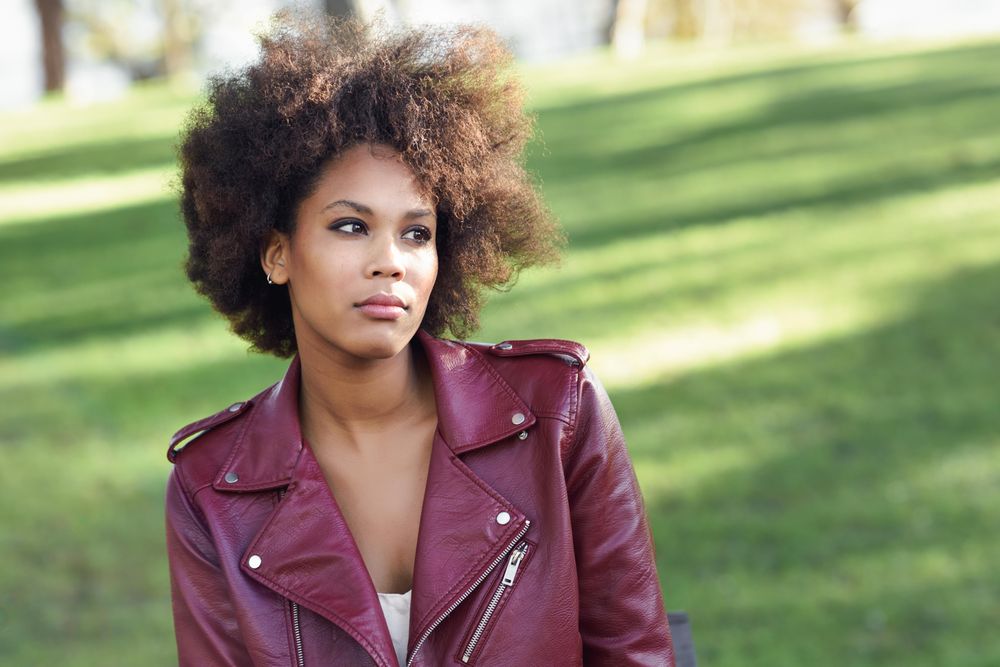 Woman sitting outside in red leather jacket on sunny day with grass in background