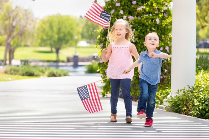 Young Sister and Brother Waving American Flags At The Park