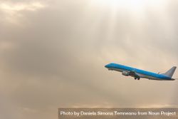 Blue airplane flying through cloudy sky with sun rays 4BgKMb