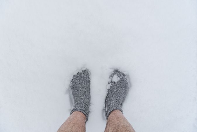 A man’s feet in socks standing on snow, above view