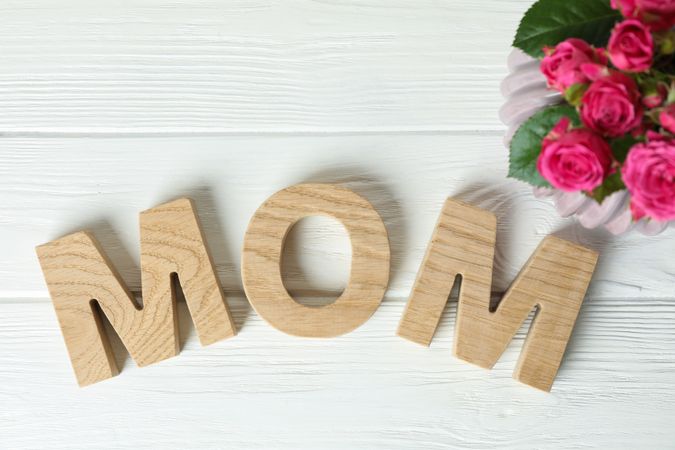 Composition with inscription Mom and pink roses on wooden background, top view