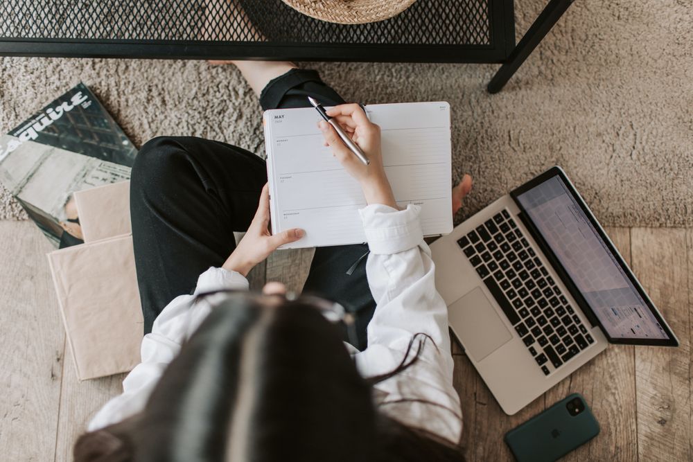Woman writing a note while using laptop sitting on floor