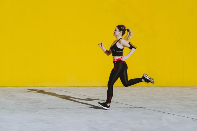 Woman with earphones running near wall