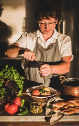 Woman in gray apron grinder pepper onto stew
