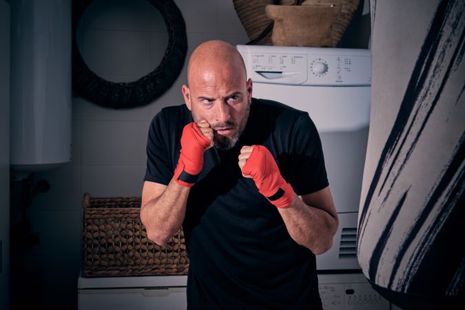 Man training boxing in the laundry room at home with a bag