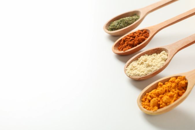 Top view of four wooden spoons full of colorful spices, copy space