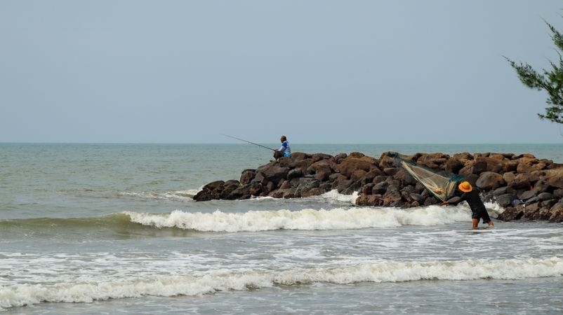 Two men fishing with fishing rod and net on the seashore