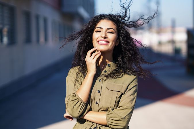 Smiling Middle Eastern woman standing outside on quiet road with hand to her chin