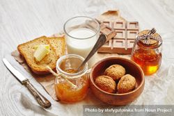 Buttered toast with milk, whole walnuts, chocolate, knife and jam on craft paper 0yleqb