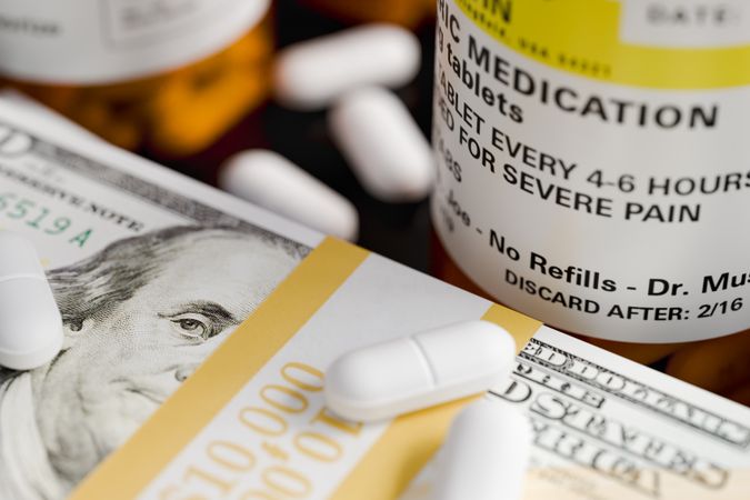 Prescription Medicine Bottles and Pills Next To Stacks of 100 Dollar Bills.
