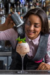 Smiling bartending adding sprinkles of powder over a prepared cocktail