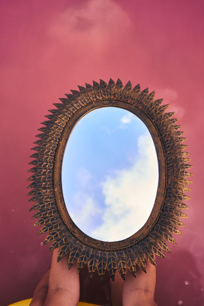 Female with decorative mirror above pink lake water