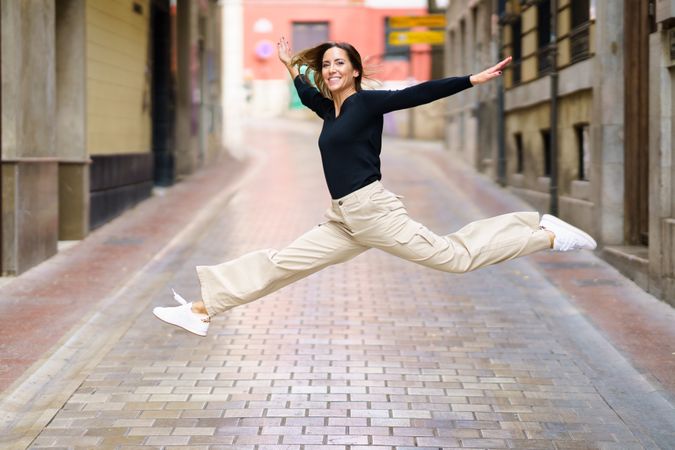 Excited woman jumping on paved street and smiling