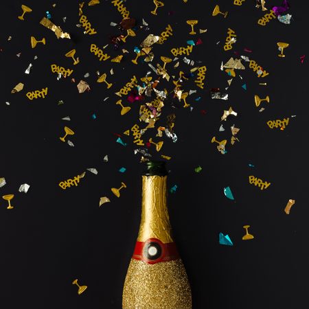 Golden champagne party bottle on background with multi-colored confetti