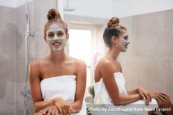 Beautiful young woman with facial mask sitting in bathroom and smiling 4BVZ34