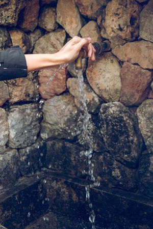 Crop of woman turning on water flowing from aged tap in nature