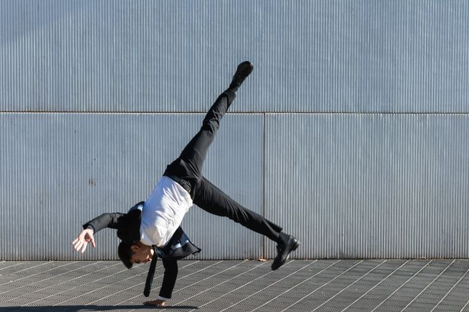 Asian businessman performing breakdance handstand on street